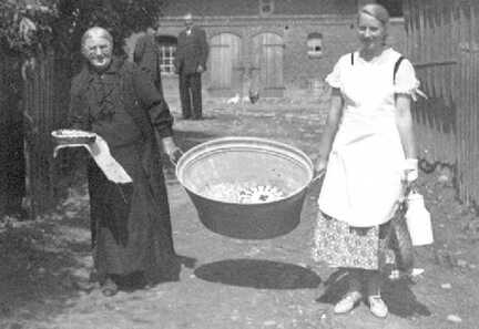 112 0007 Oma Lange und Martha Augustin tragen eine Wanne mit Kuchen Oma Lange hat fuer alle Feierlichkeiten im Dorf den Kuchen gebacken